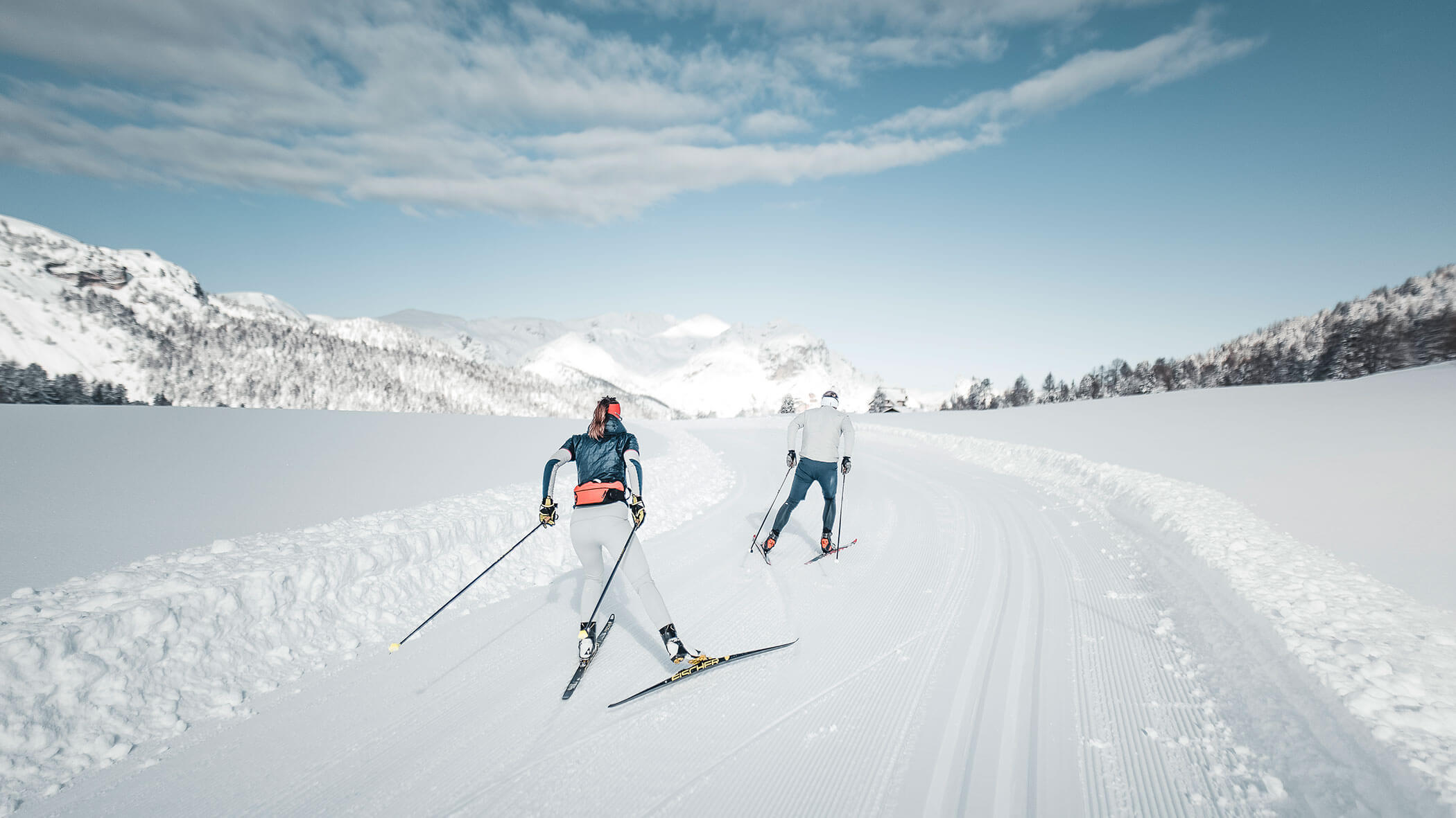 Due persone praticano sci di fondo su una pista innevata.