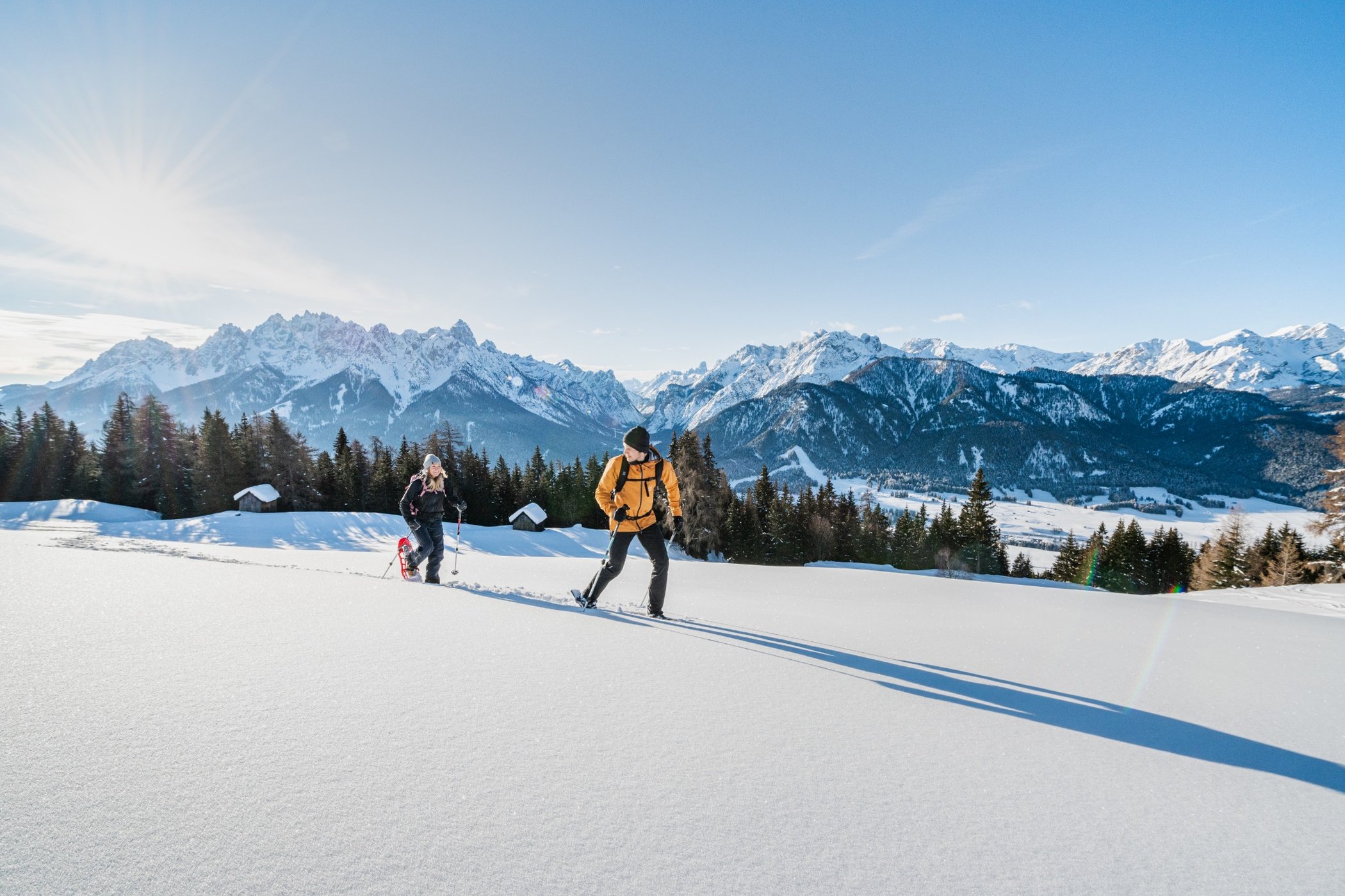 Due persone stanno facendo un'escursione su un terreno innevato, con le montagne in lontananza.
