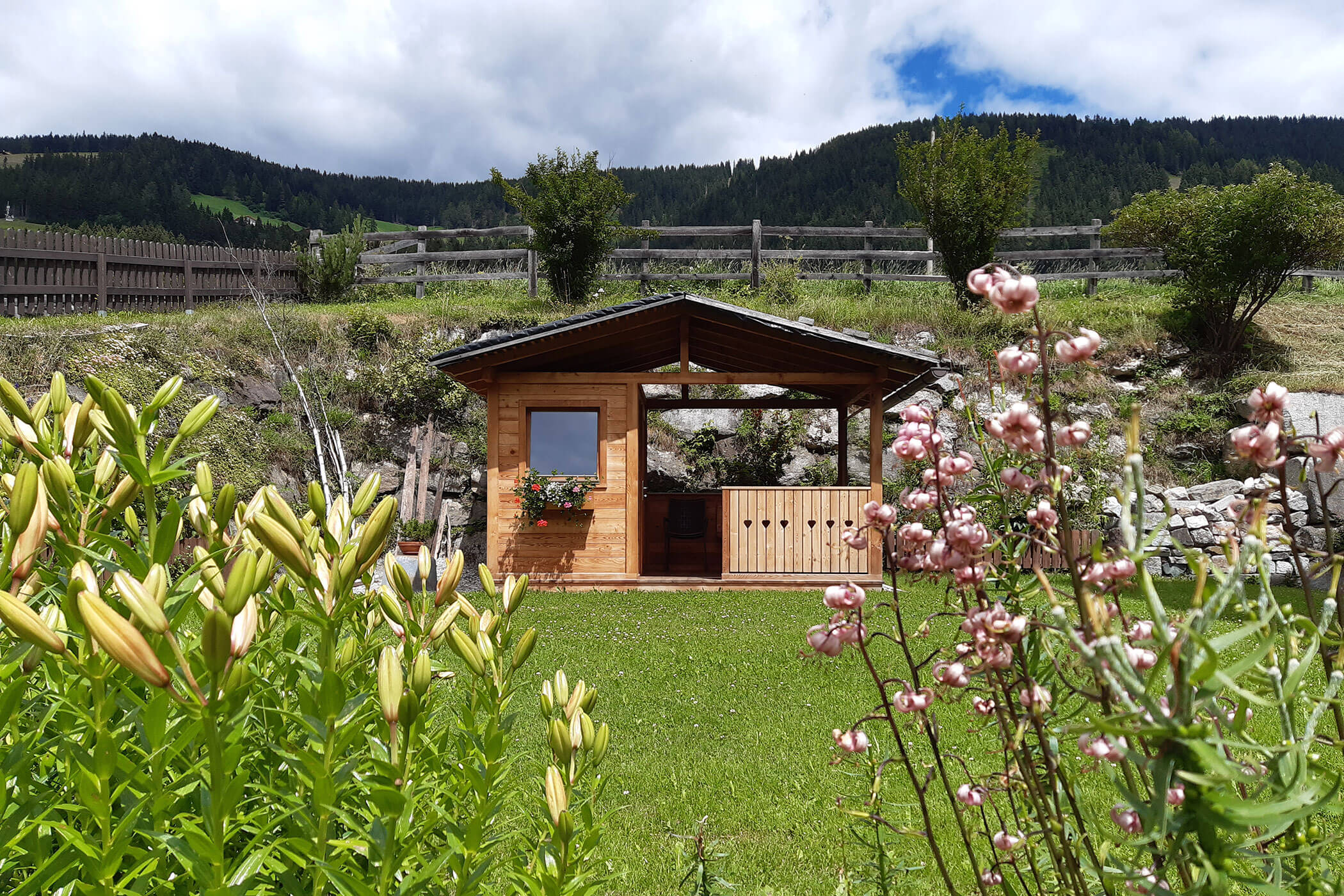 Una piccola casetta da giardino si trova in mezzo a un campo, circondata da un prato verde e da un cielo azzurro.